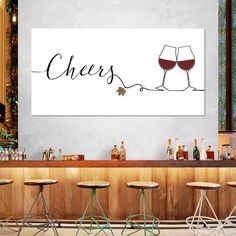 a bar with three stools and two wine glasses on the wall above it that says cheers