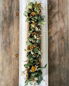 an arrangement of flowers and greenery is displayed on a wooden table with white linen