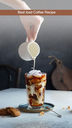 someone pouring milk into a glass filled with ice cream and toppings on top of a table