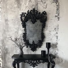 a black table with a mirror and vase on it in front of a white wall