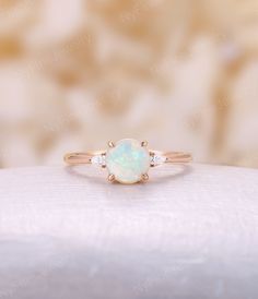 a white opal and diamond ring sitting on top of a cushion