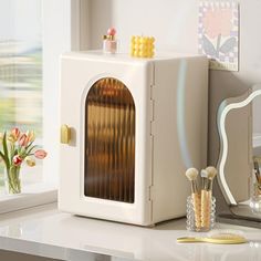 a small white cabinet sitting on top of a counter next to a mirror and brush