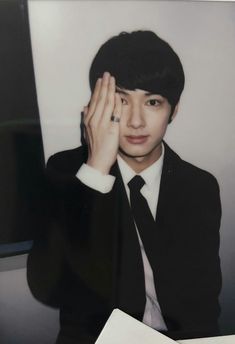 a young man in a suit and tie holding his hand to his face while sitting at a desk