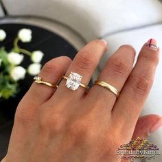 a woman's hand with two gold rings on it and a white flower in the background