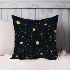 a black pillow with gold stars and planets in the sky on top of a fluffy white blanket