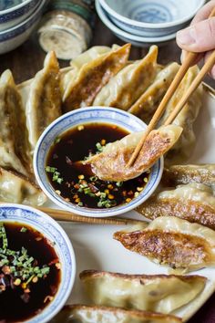 a person holding chopsticks over some dumplings on a plate with dipping sauce