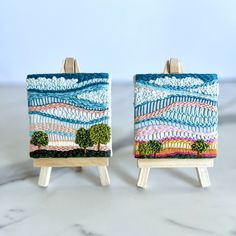 two miniature easels with paintings on them sitting on a table top next to each other