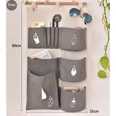 a wall hanging organizer with three pockets and sunglasses on it next to a potted plant