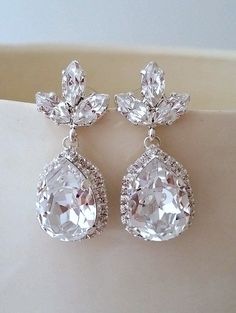 a pair of earrings with white stones and clear crystals on the bottom, sitting on a piece of cloth