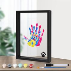 a hand print is on the wall next to some paints and markers, with a dog's paw in the background