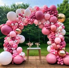 a pink and white balloon arch with balloons on the top is set up for an outdoor party