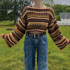 a woman standing on top of a lush green field wearing jeans and a knitted sweater