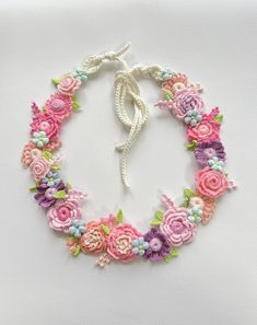 a crocheted necklace with flowers is shown on a white surface and has a knot in the middle