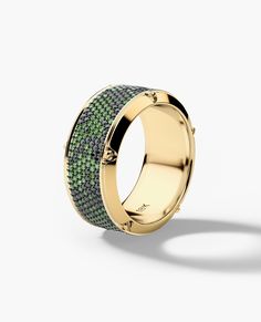 an 18k yellow gold ring with green and white diamonds, set on a plain surface