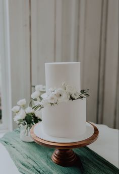 a white wedding cake sitting on top of a wooden stand next to flowers and greenery