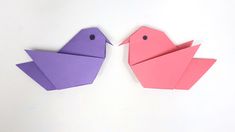 two origami birds sitting next to each other on a white surface, one pink and the other purple