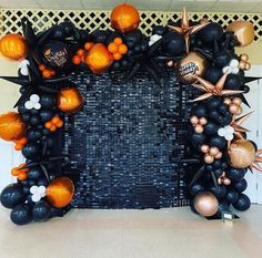 a black and gold balloon arch decorated with oranges, white and black balloons in the shape of bats