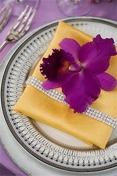 a purple flower is on top of a plate with silverware and napkins in front of it