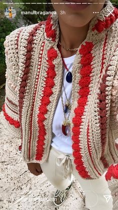 a woman is wearing a crocheted cardigan and white pants with red trim