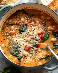 a bowl of soup with spinach, beans and cheese on the table next to bread