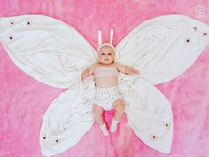 a baby laying on top of a pink blanket covered in white butterfly shaped blankets and pillows