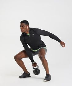 a man is squatting while holding a kettle in one hand and lifting the other