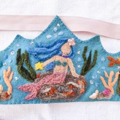 an embroidered mermaid sitting on top of a rock with corals and other sea creatures