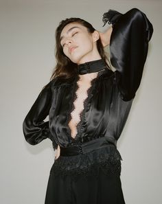 Our Rita Blouse in black features a plunging V neckline trimmed with delicate Venise lace, a true waistline cinch and soft billowing sleeves all trimmed with Alençon lace and embroidered ruffled tulle lace. 100% Silk Charmeuse lined with Silk Habutai Three satin covered pearl buttons for each closure Dry clean only Each piece is made to order and handcrafted in our atelier. Slight variations may occur as each piece is unique. Chic Evening Tops With Lace Bodice, Feminine Lace Top With Lace Sleeves For Evening, Evening Lace Top With Ruffles, Ruffled Lace Evening Top, Ruffled Lace Top For Evening, Lace Top With Ruffles For Evening, Elegant Lace Collar Top For Parties, Elegant Lace Blouse For Date Night, Evening Fitted Lace Top With Ruffles