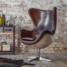 a brown leather chair sitting on top of a wooden floor next to a brick wall