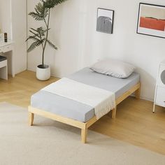 a bed sitting in a bedroom next to a white dresser and table with a potted plant on it