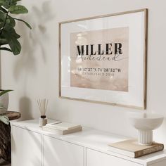 a white dresser with a framed poster on the wall above it and a plant next to it