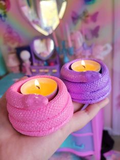 two pink and purple candles sitting on top of each other in front of a mirror