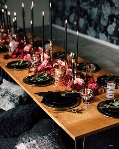 a long wooden table topped with black plates and candles