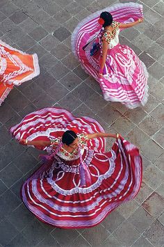 three women in red and white dresses are dancing on the street with umbrellas over their heads