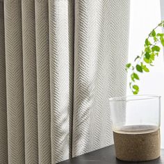 a close up of a vase on a table near a window with a curtain in the background