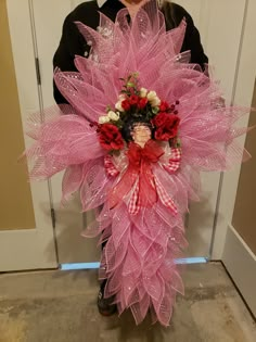 a woman standing in front of a door holding a pink wreath with flowers on it