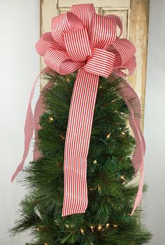 a red and white bow on top of a christmas tree in front of a door