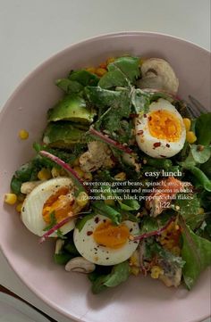 a pink bowl filled with salad topped with hard boiled eggs and vegtables