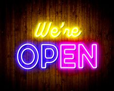 we're open neon sign on wooden wall