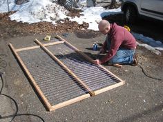 a man kneeling down next to a metal grate on the ground in front of a car