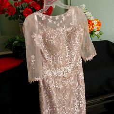 a white dress hanging on a rack in front of flowers and a vase with red roses