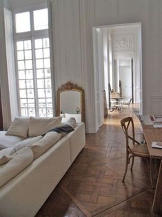 a living room filled with furniture next to a wooden table and chairs in front of two windows