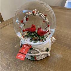 a snow globe with two red birds in it on top of a wooden table next to a price tag