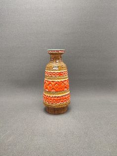 an orange and yellow vase sitting on top of a gray table next to a wall