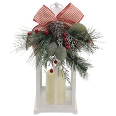 a candle with pine cones, berries and mists on it in a white lantern holder