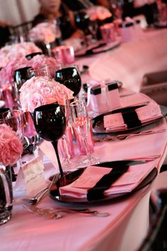 the table is set with pink flowers and black wine glasses