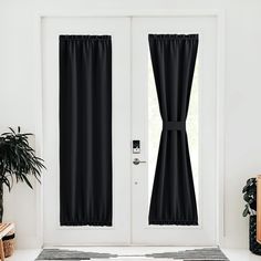 black curtains hanging on the side of a white door in front of a potted plant