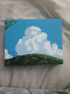 a painting of a tree on a hill with clouds in the blue sky above it