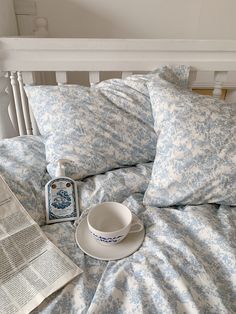 a cup and saucer sitting on top of a bed next to an open newspaper