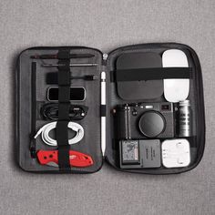 an open black case with various items in it on a gray surface, including electronics and cords